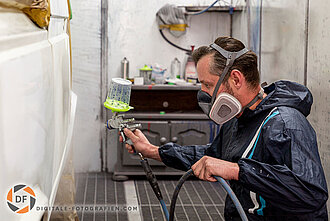 Lackierer im Anzug in der Lackierkabine bei der Arbeit Lackierer