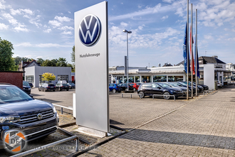 Autohaus mit Volkswagen Logo im Vordergrund. Volkswagen Logo